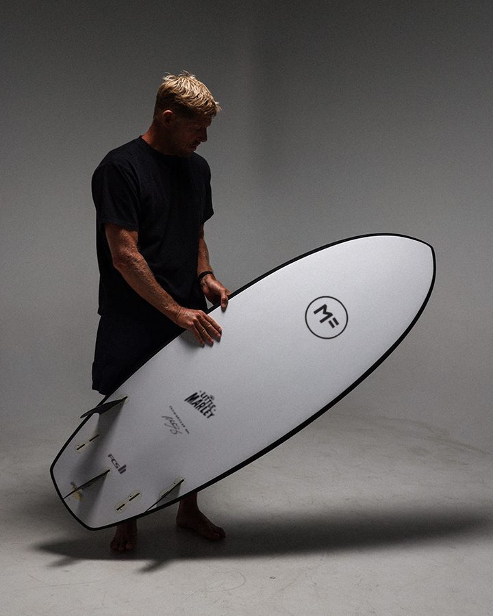 Mick Fanning holding a white MF Little Marley softboard in the studio